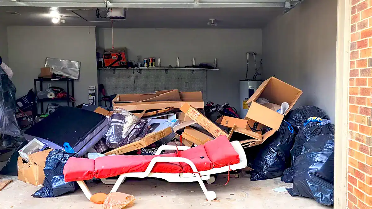 Cluttered garage filled with furniture, bags, and household junk ready for a garage cleanout.