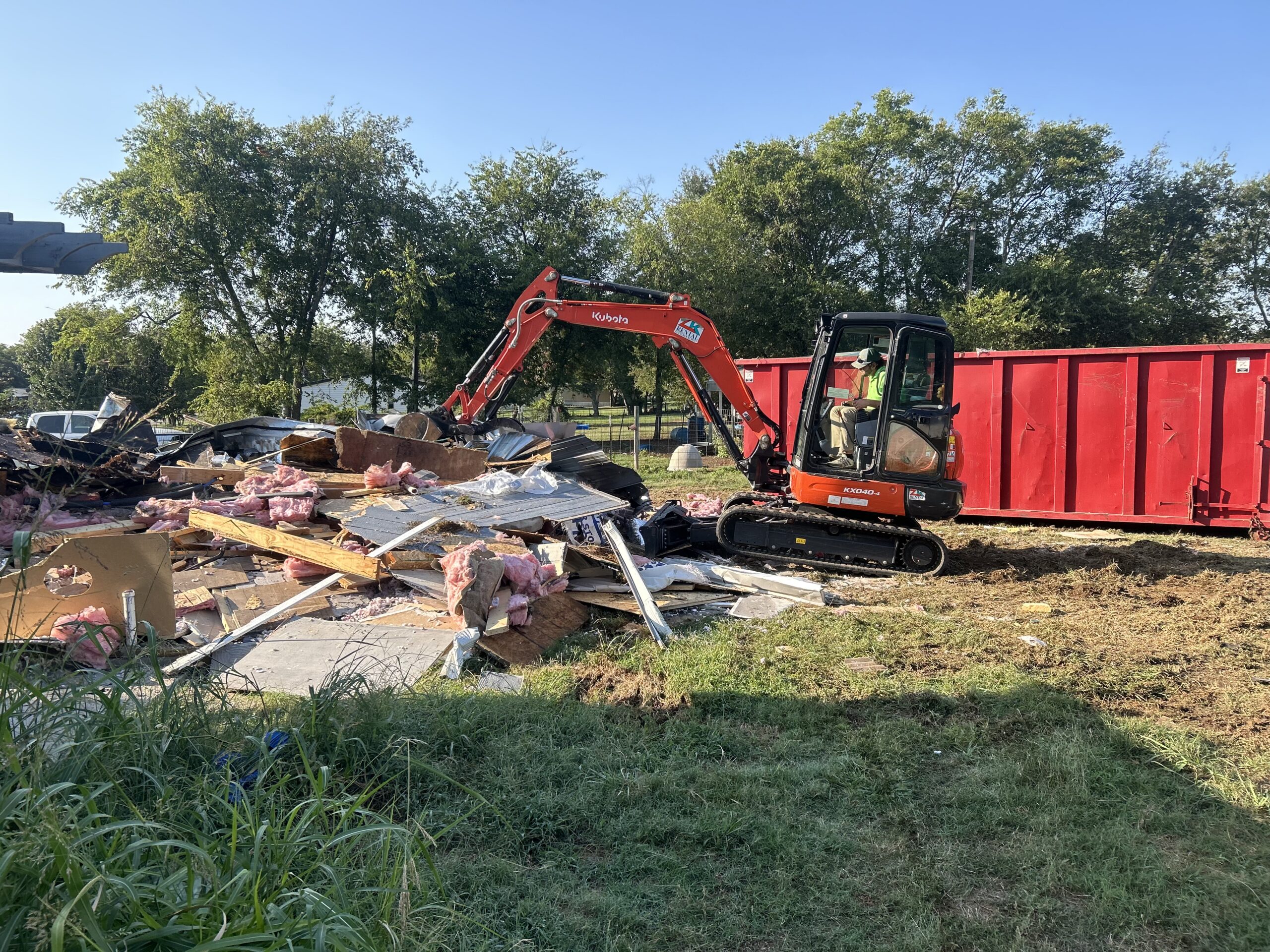Excavator loading renovation debris into a dumpster during construction cleanup.
